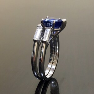 May include: A silver ring set with a blue sapphire and two baguette-cut diamonds. The ring is engraved with the word "MADE".