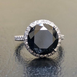 May include: A black diamond engagement ring with a halo of smaller diamonds set in white gold.
