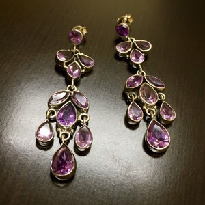 May include: A pair of dangle earrings with multiple purple amethyst stones. The earrings are silver and have a teardrop shape.