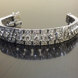 Puede incluir: Un brazalete de plata con una fila de diamantes redondos grandes engastados en pav&eacute;. El brazalete est&aacute; hecho de metal y tiene un acabado pulido.