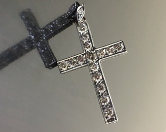 May include: A silver cross pendant with a diamond-encrusted design. The cross is set with small, clear diamonds that create a sparkling effect.