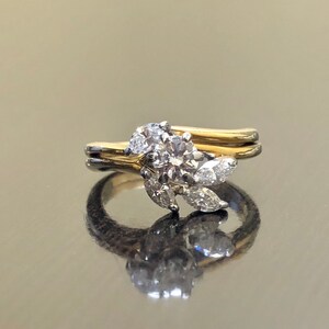 May include: A gold and silver engagement ring with a round center diamond and smaller diamonds set in a leaf design.