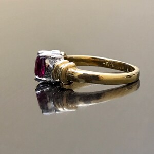 May include: A gold ring with a pink gemstone and two smaller white gemstones. The ring is set in a twisted band.