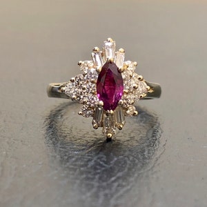 May include: A gold ring featuring a large, marquise-shaped ruby surrounded by a cluster of smaller diamonds.