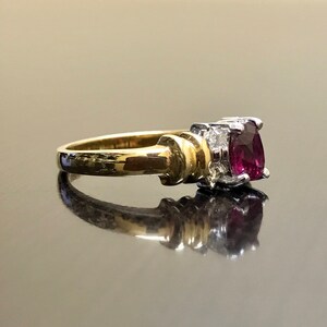 May include: A gold ring with a large, dark red gemstone surrounded by smaller, clear gemstones.