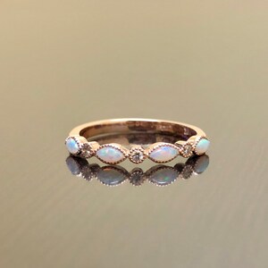 May include: A delicate rose gold band ring with five oval-shaped white opals and small diamonds set in the band.