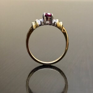 May include: A gold and silver ring with a red gemstone and smaller white gemstones.