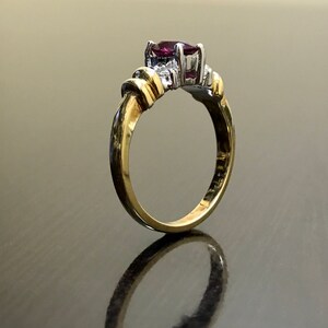 May include: A gold ring with a purple gemstone and smaller white gemstones. The ring is set on a dark surface.