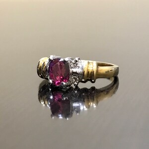 May include: A gold and silver ring with a large, oval-shaped, purple gemstone. The ring has a textured band.