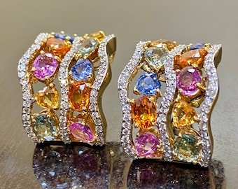 May include: A pair of gold earrings with a wave design featuring a variety of colorful gemstones, including pink, blue, yellow, and green sapphires, and diamonds.