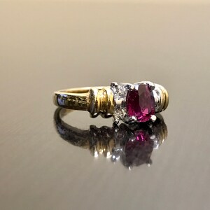 May include: A gold and silver ring with a large oval-shaped ruby gemstone surrounded by smaller diamonds.