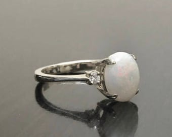May include: A silver ring with a white opal gemstone and two smaller white gemstones on the band.