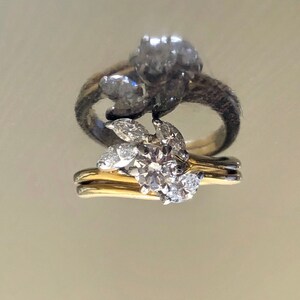 May include: A pair of gold and silver engagement rings with a large round diamond and smaller diamonds set in a leaf design.