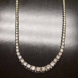 May include: A silver necklace with a row of round, clear stones. The necklace is on a dark background.