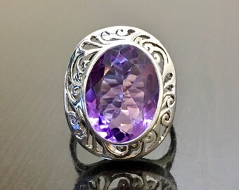 May include: A silver ring with an oval-shaped amethyst gemstone set in a filigree design.