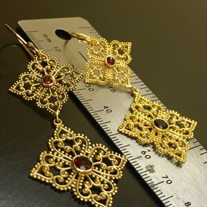 May include: Gold filigree earrings with red gemstone accents. The earrings are shown next to a ruler, measuring approximately 3.8 cm in length.