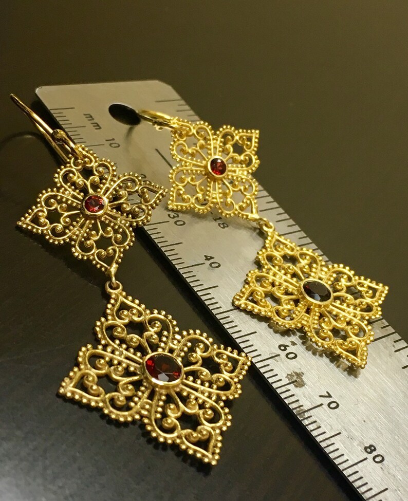 May include: Gold filigree earrings with red gemstone accents. The earrings are shown next to a ruler, measuring approximately 3.8 cm in length.
