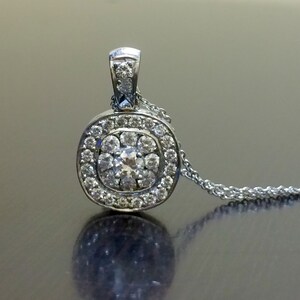 May include: A silver pendant necklace with a round, square-shaped pendant set with small diamonds. The pendant has a central diamond surrounded by a halo of smaller diamonds.
