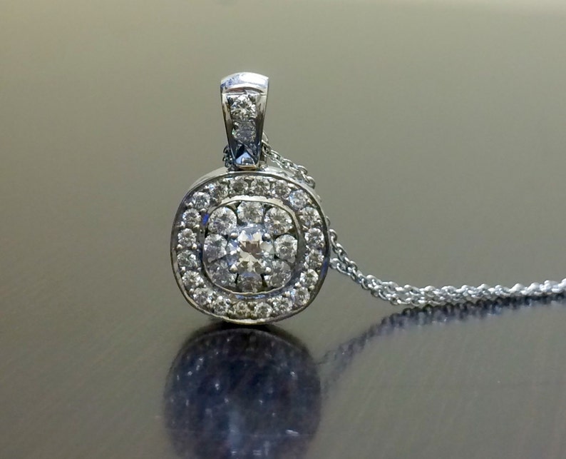 May include: A silver pendant necklace with a round, square-shaped pendant set with small diamonds. The pendant has a central diamond surrounded by a halo of smaller diamonds.