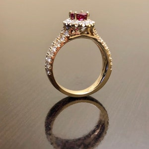 May include: A gold ring with a red gemstone surrounded by smaller white gemstones. The ring has a band of smaller white gemstones.
