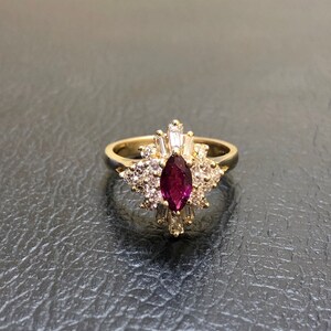 May include: A gold ring featuring a large, dark purple gemstone surrounded by smaller, clear gemstones.