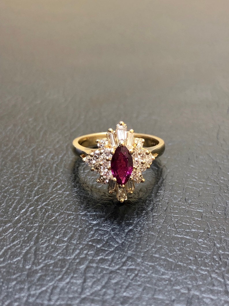 May include: A gold ring featuring a large, dark purple gemstone surrounded by smaller, clear gemstones.