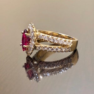 May include: A gold ring with a marquise-shaped ruby surrounded by a halo of smaller diamonds. The ring has a split shank with a row of diamonds on each side.