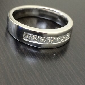 K&ouml;nnte beinhalten: Ein silberner Ring mit einer Reihe kleiner, klarer, quadratischer Diamanten, die in einer Kanalfassung gefasst sind.