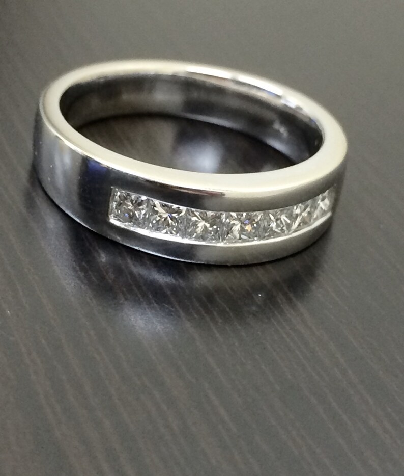 K&ouml;nnte beinhalten: Ein silberner Ring mit einer Reihe kleiner, klarer, quadratischer Diamanten, die in einer Kanalfassung gefasst sind.