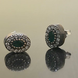 May include: A pair of silver earrings with a green oval stone surrounded by small white stones.