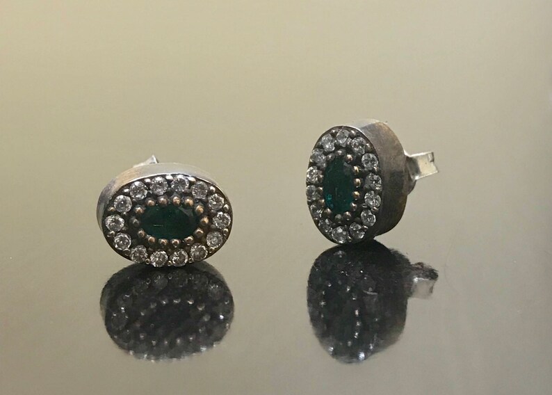 May include: A pair of silver earrings with a green oval stone surrounded by small white stones.