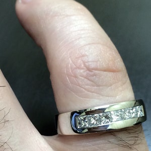 K&ouml;nnte beinhalten: Ein silberner Ring mit einer Reihe quadratischer Diamanten, die in einer Kanalfassung gefasst sind.