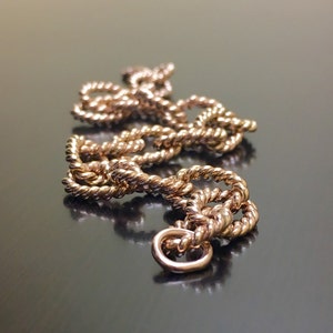 Puede incluir: Un collar de cadena dorado con un dise&ntilde;o de cuerda. La cadena est&aacute; trenzada y tiene un cierre en el extremo.