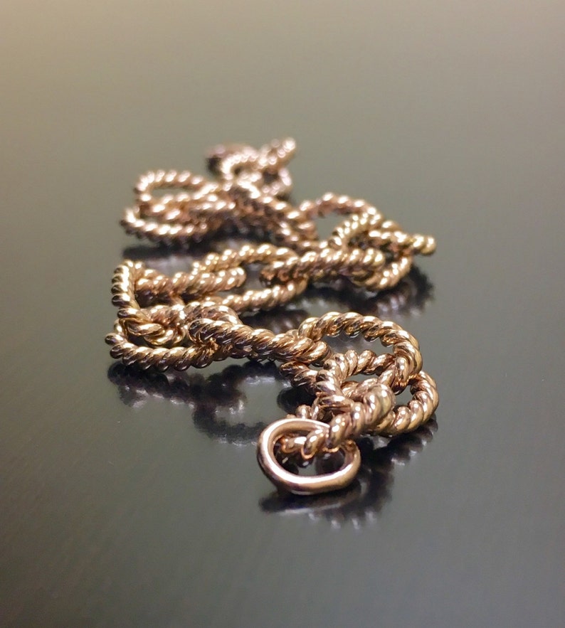 Puede incluir: Un collar de cadena dorado con un dise&ntilde;o de cuerda. La cadena est&aacute; trenzada y tiene un cierre en el extremo.
