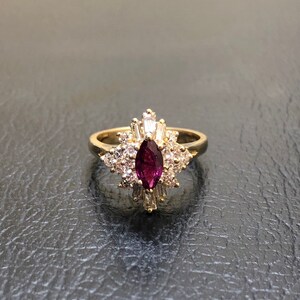Op de afbeelding: Een gouden ring met een grote, marquise-vormige robijn omringd door kleinere diamanten. De ring heeft een delicaat, bloemig ontwerp.