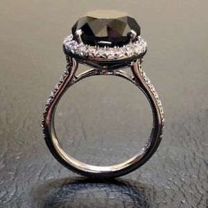 May include: A black diamond engagement ring with a halo of smaller diamonds set in a white gold band.