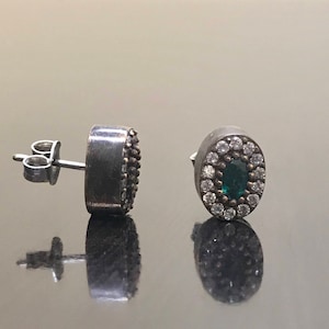 May include: A pair of silver earrings with a green gemstone surrounded by white stones.