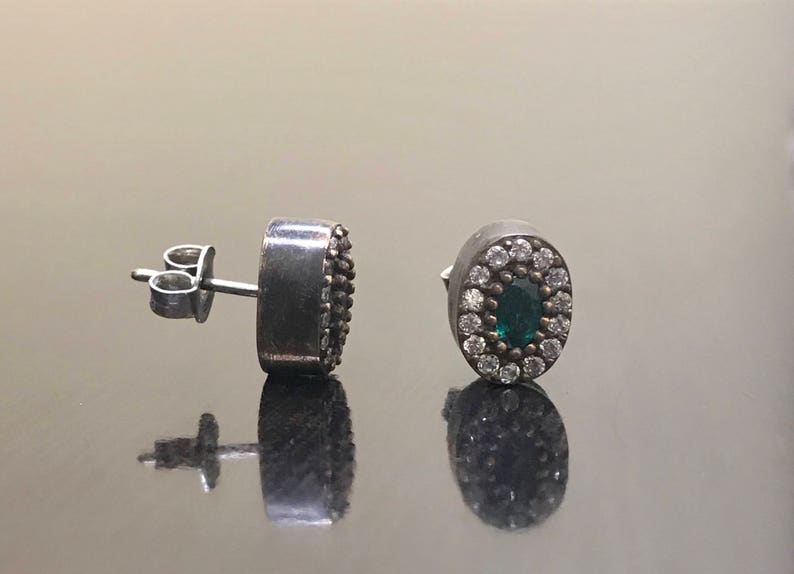 May include: A pair of silver earrings with a green gemstone surrounded by white stones.