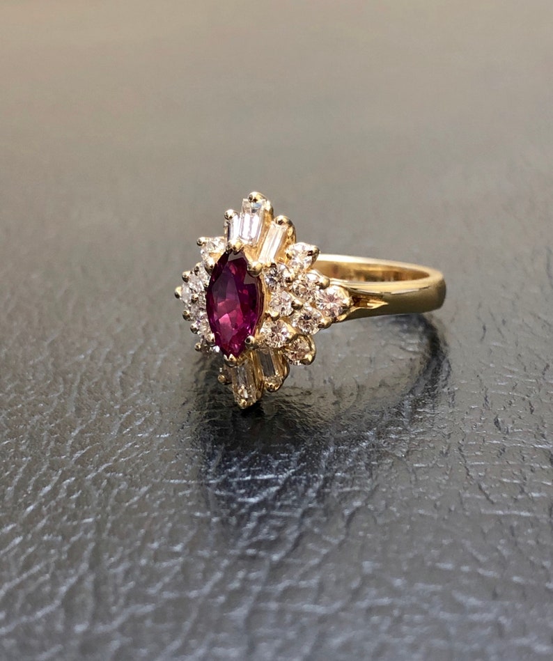 May include: A gold ring featuring a large, oval ruby surrounded by smaller diamonds. The ring has a delicate, floral design.