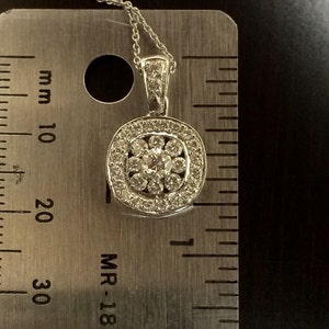 May include: A silver pendant necklace with a round, multi-faceted diamond center stone surrounded by smaller diamonds. The pendant is approximately 1.5 cm in diameter and is measured against a ruler.