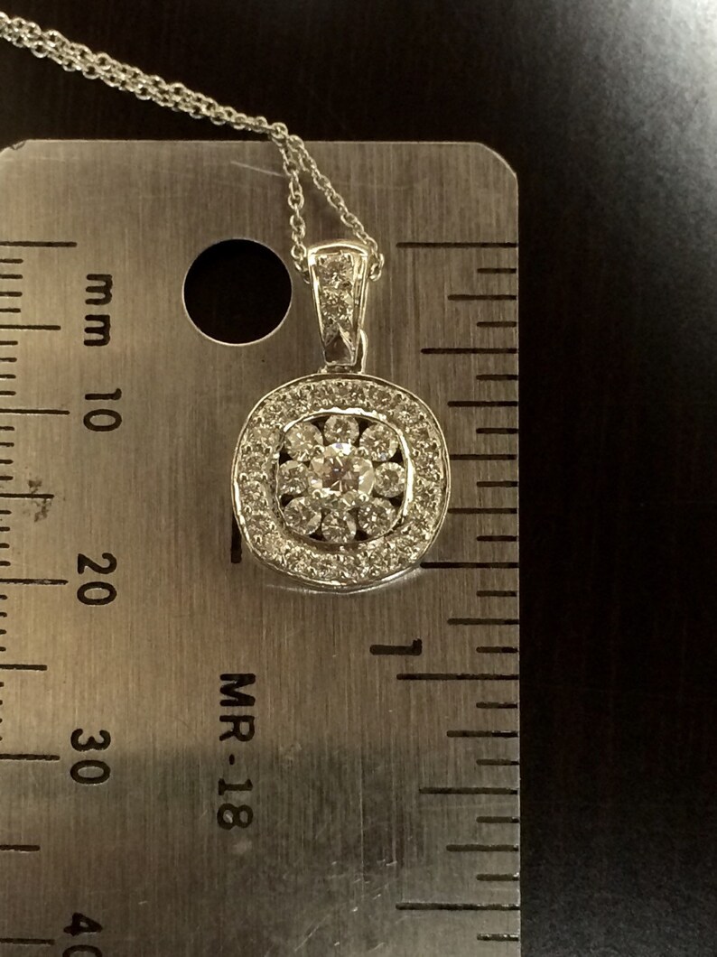May include: A silver pendant necklace with a round, multi-faceted diamond center stone surrounded by smaller diamonds. The pendant is approximately 1.5 cm in diameter and is measured against a ruler.
