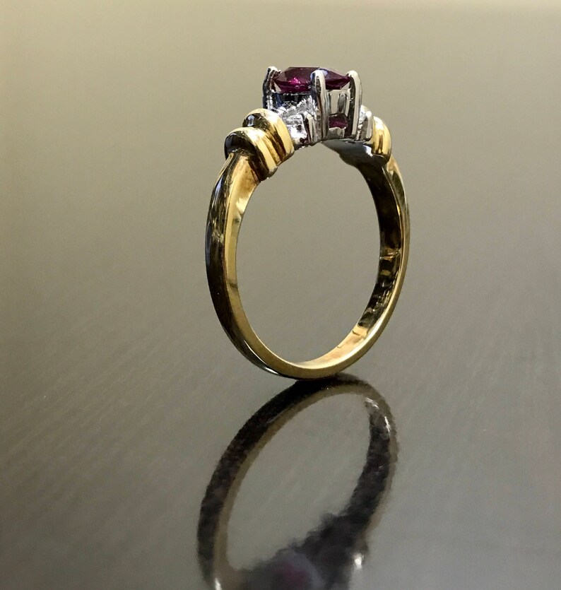 May include: A gold ring with a purple gemstone and smaller white gemstones. The ring is set on a dark surface.