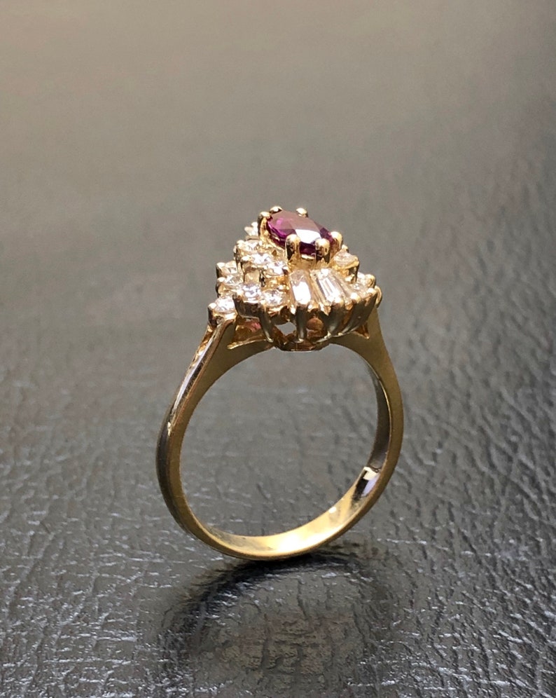 Op de afbeelding: Een gouden ring met een grote, ovale, paarse edelsteen omringd door kleinere, heldere edelstenen.