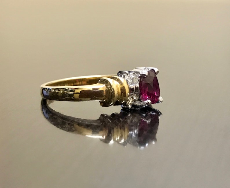 May include: A gold ring with a large, dark red gemstone surrounded by smaller, clear gemstones.