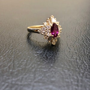 May include: A gold ring featuring a large pear-shaped ruby surrounded by smaller diamonds. The ring has a delicate, floral design.