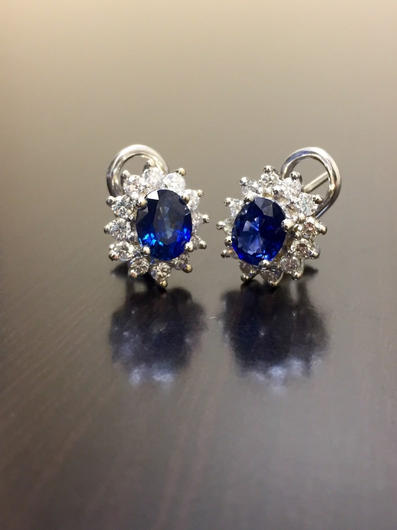 May include: A pair of silver earrings with a blue sapphire gemstone surrounded by a halo of smaller diamonds.