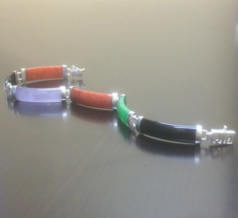 May include: A silver bracelet with four different colored jade stones. The stones are green, black, purple, and orange. The bracelet has a silver clasp.