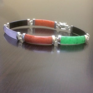 May include: A bracelet with four different colored stones. The stones are black, purple, red, and green. The bracelet is made of silver.