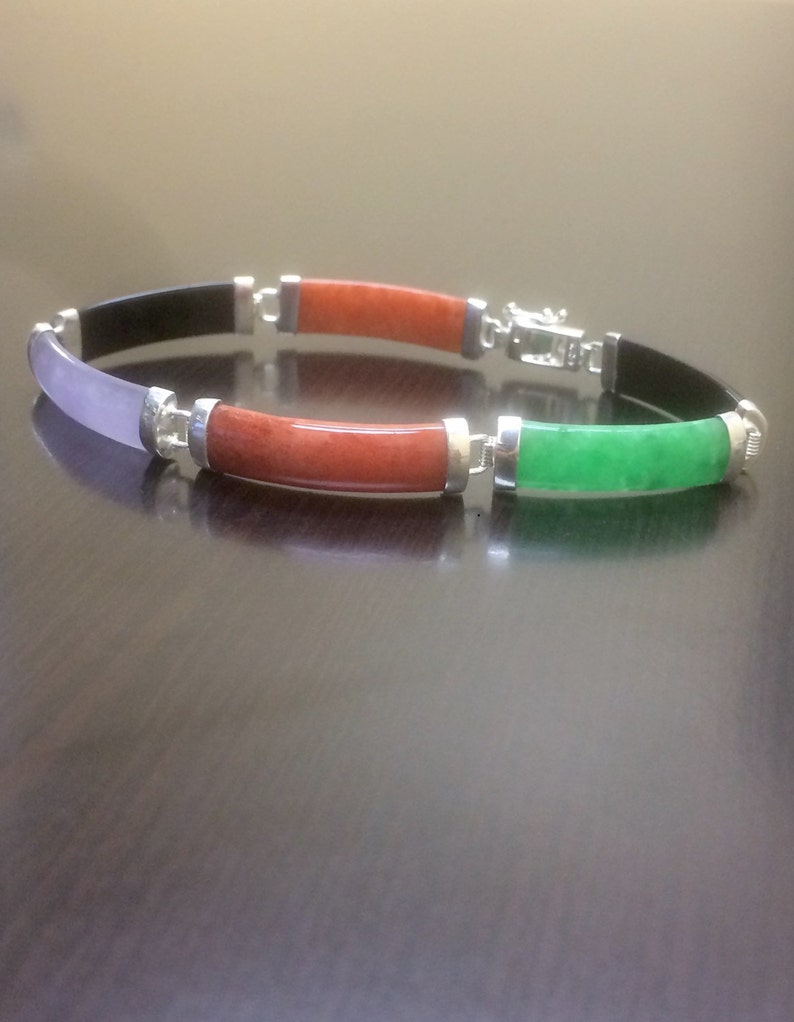 May include: A bracelet with four different colored stones. The stones are black, purple, red, and green. The bracelet is made of silver.