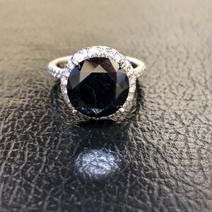 May include: A black diamond engagement ring with a halo of smaller diamonds set in a white gold band.
